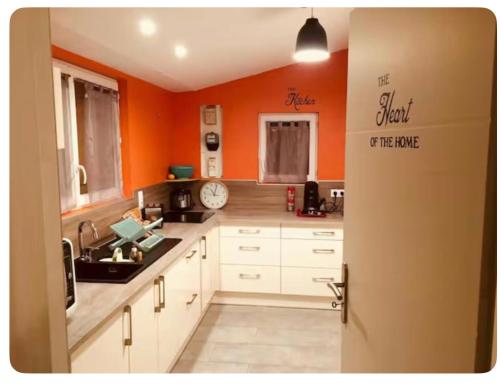 - une cuisine avec des murs orange et des armoires blanches dans l'établissement La Maison Téranga au Bourg de Villenave, à Courrejean