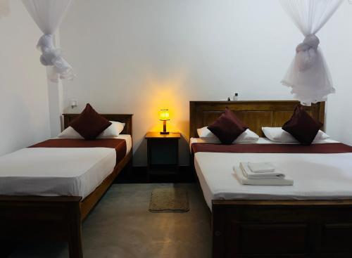 two beds in a room with a lamp on a table at The Wild Elephant Resort in Sigiriya