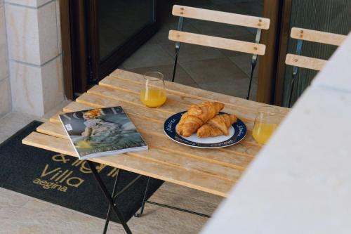 a table with a plate of croissants and orange juice at Seaside "Stone & Light Villa II" close to Aegina City in Khlóï
