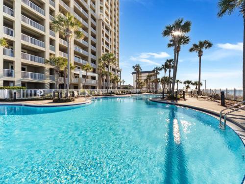 a large swimming pool with palm trees in front of a building at Grand Panama Resort - Ocean Views, Heated Pool & Tub 3 BR 3 Full BA Sleeps 10 in Panama City Beach