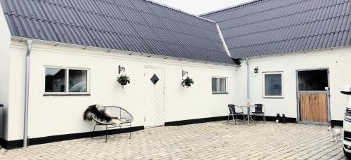 a white building with a black roof and chairs at Ferielejlighed i landlige omgivelser in Ørsted