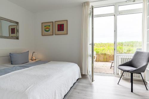 a bedroom with a bed and a chair and a window at Dünennest in Südstrand