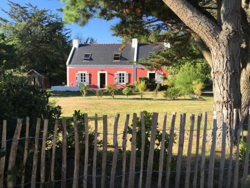 une maison rouge derrière une clôture avec un arbre dans l'établissement Longère traditionelle Keroulep, à Belle-Île-en-Mer