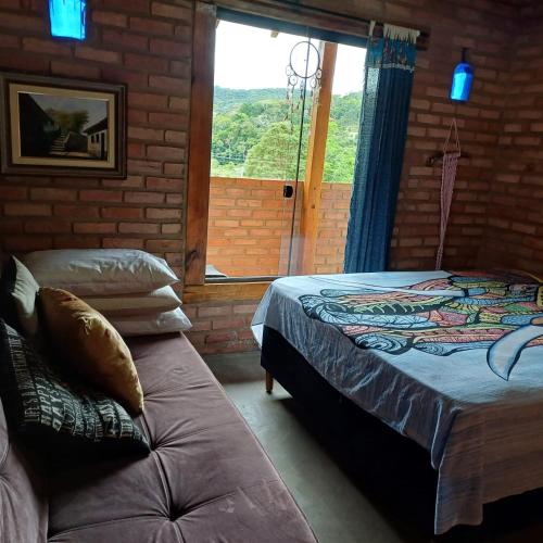 a bedroom with a bed and a couch and a window at Claudinha chalés in Conceição da Ibitipoca