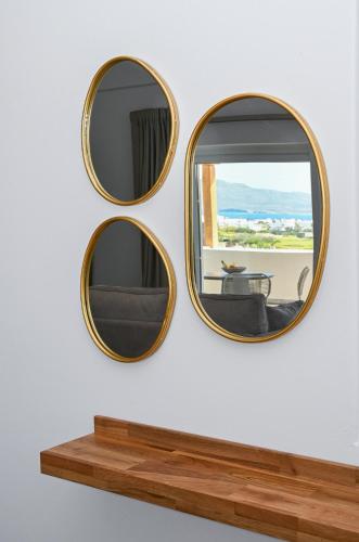 two round mirrors on a wall with a wooden shelf at Olive - Volia deluxe apartments in Adamas