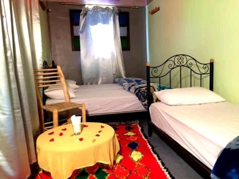 a room with two beds and a table with a tableablish at Gite Likemte Tachdirt in Tacheddirt