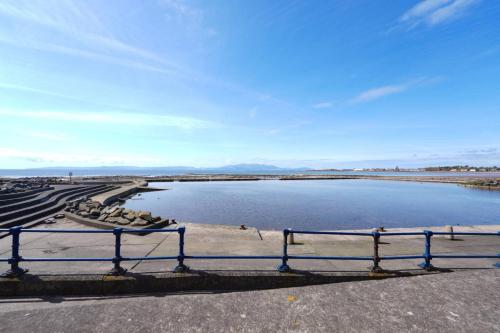 a bench sitting next to a body of water at Caledonia by the Sea in Saltcoats