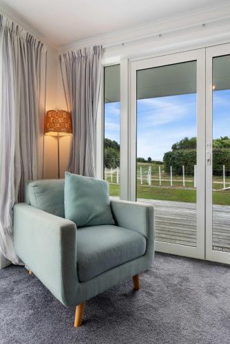 a blue chair in a room with windows at WaveSong Cottage - Your Escape by the Sea in Parapara 