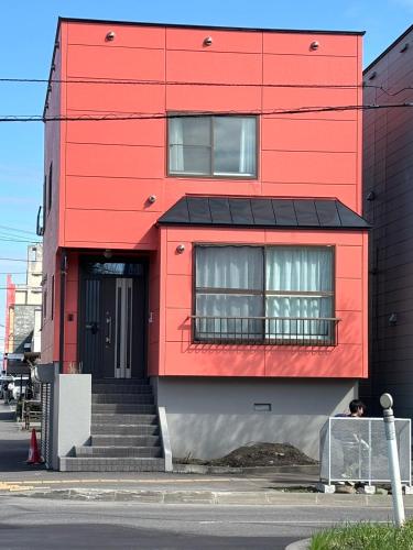 a red building with a black door and stairs at Stay In Miyashita in Asahikawa