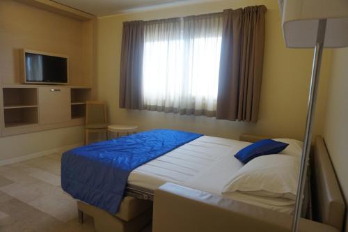 a bedroom with a bed with a blue blanket and a window at Hotel Columbus in Lignano Sabbiadoro