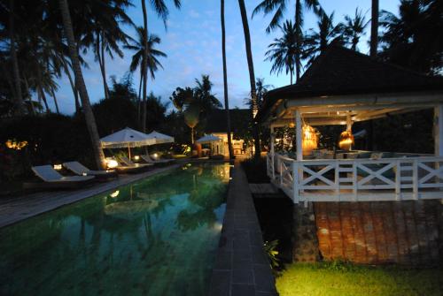 a swimming pool with a building and palm trees at night at Beach Villa Pantai Matanai in Tianyar