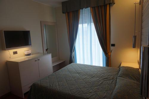 a bedroom with a bed and a tv and a window at Hotel Columbus in Lignano Sabbiadoro