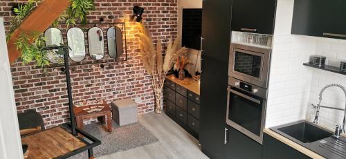 une cuisine avec des armoires noires et un mur en briques dans l'établissement Maison de village Cosy, à Villelongue-de-la-Salanque