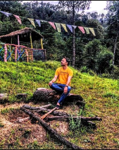 a man sitting on a rock in a field at The Chakras Valley Homestay in Binsar