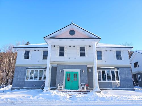 a white house with a green door in the snow at guest house White House ホワイト ハウス in Shimukappu