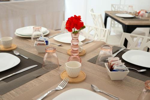 a table with white plates and a red flower in a vase at From Flori in Terrasini