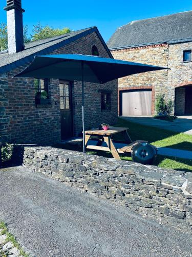 a picnic table with an umbrella in front of a house at L Abri douillet in Libin