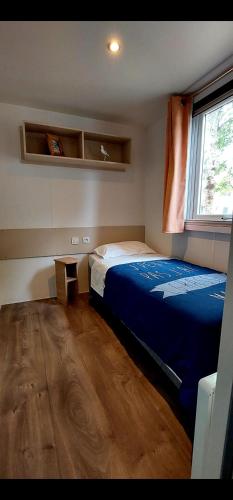 une chambre avec un lit bleu et une fenêtre dans l'établissement Mobil Home Camping Les VIVIERS, Claouey, à Claouey