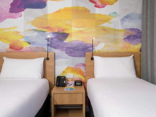 two beds in a room with a colorful wall at Ibis Styles Hobart in Hobart