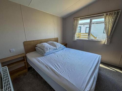 a bedroom with a bed with white sheets and a window at Beautiful 6 Berth Caravan With Stunning Sea Views In Suffolk Ref 68029Cr in Lowestoft