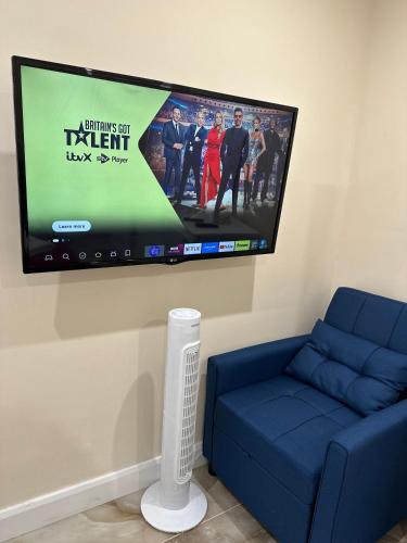 a flat screen tv hanging on a wall with a blue couch at Modern Studio Luxe Heathrow London in New Bedfont