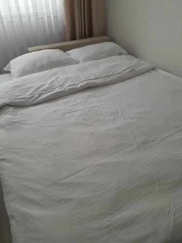 an unmade bed with white sheets and pillows at City Center Moku Apartman in Zenica