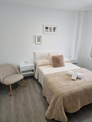 a white bedroom with two beds and a chair at Apartamento Calma in Negreira