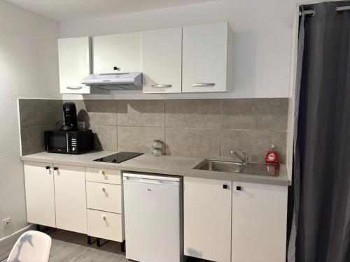 une cuisine avec des armoires blanches et un évier dans l'établissement Appartement cosy, terrasse privée, parking, centre ville, à Mont-de-Marsan