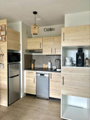 - une cuisine avec des placards en bois et un lave-vaisselle blanc dans l'établissement Studio cosy à 1mn de la mer, jardin et parking privé, à Saint-Jean-de-Monts