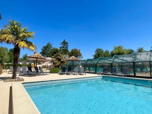 une piscine avec un palmier et un bâtiment dans l'établissement Camping Les Tourterelles, à Rang-du-Fliers