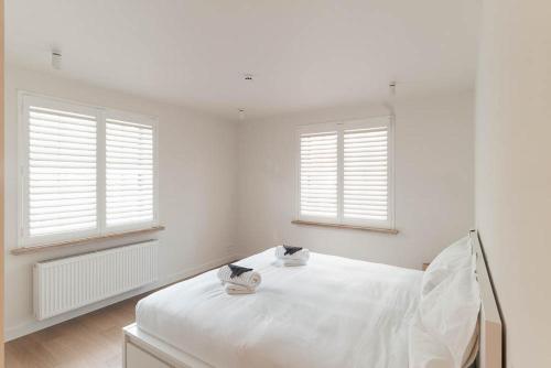 a white bedroom with two windows and a bed at Villa 'La Mer Veille - Bécassine' in Oostduinkerke - Bad in Oostduinkerke