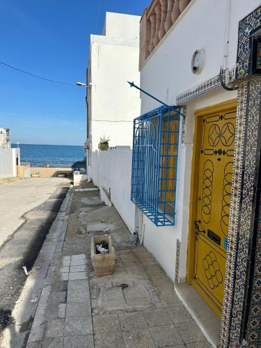 a narrow street with a yellow door and the ocean at Des appartements a la Marsa plage Pieds dans l'eau in Dar Salah Bey