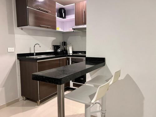 a kitchen with a black counter and two white chairs at Apto Botero 704 - WAIWA HOST in Bucaramanga