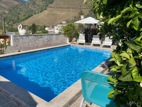 a blue swimming pool with white chairs and a hill at Casa Nunes in Pinhão