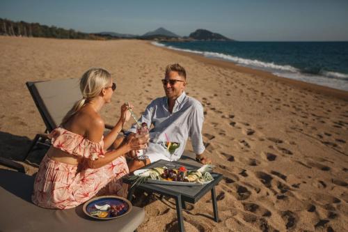a man and woman sitting on the beach with a tray of food at The Westin Resort, Costa Navarino in Romanós