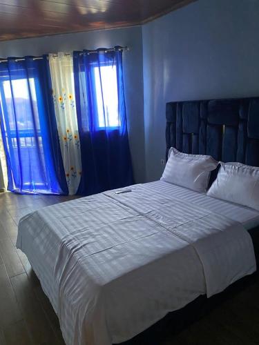 una camera da letto con un grande letto bianco con tende blu di Melvas home a Douala