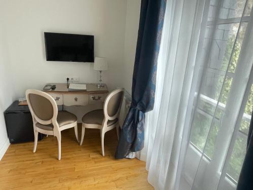 a room with a desk with two chairs and a television at Hôtel Victor Hugo in Pontorson