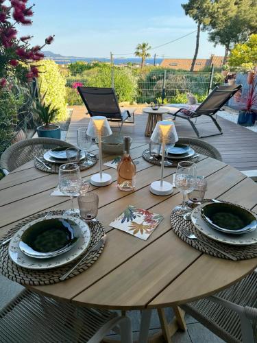 - une table en bois avec des assiettes et des verres sur la terrasse dans l'établissement T2 neuf avec sa magnifique vue mer sur la baie de Bandol, à Bandol