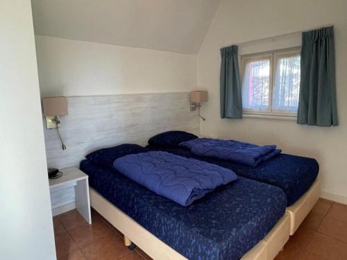 a bedroom with a bed with blue sheets and a window at Bungalow in Haaksbergen near Nature Trails in Haaksbergen
