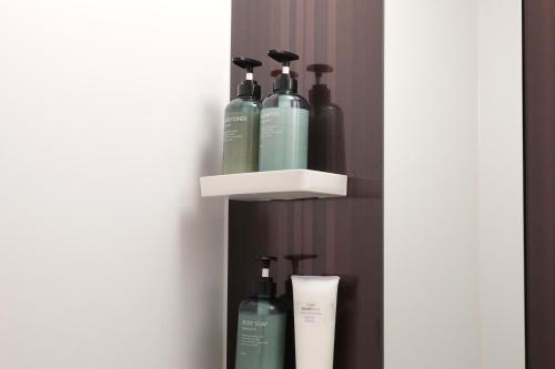 a shelf with three bottles of soap on a wall at ROOMs 003 カフェ併設 綺麗なワンルーム 分倍河原駅から徒歩3分 in Fuchu