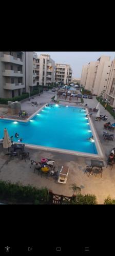 a large swimming pool with tables and chairs and buildings at شاليه للايجار 3 غرف مكيفات بقرية جراند هيلز الساحل الشمالى بإطلاله مباشره على البول in Qaryat Shurūq