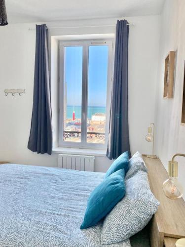 une chambre avec un lit avec des oreillers bleus et une fenêtre dans l'établissement Le Rayon Vert vue mer, à Fécamp
