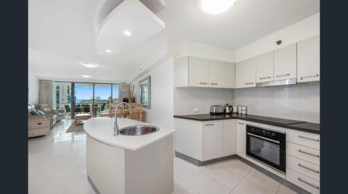 a kitchen with white cabinets and a sink and a living room at Cilento Mooloolaba in Mooloolaba