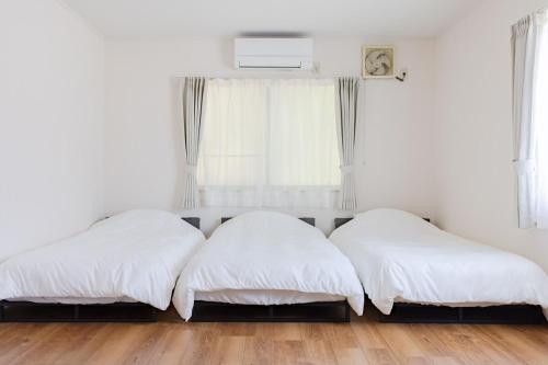 two beds in a room with white walls and wood floors at Shima Yadori in Oshima
