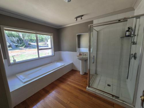 a bathroom with a shower and a tub and a window at Cozy FarmStay with Spa in Pokeno