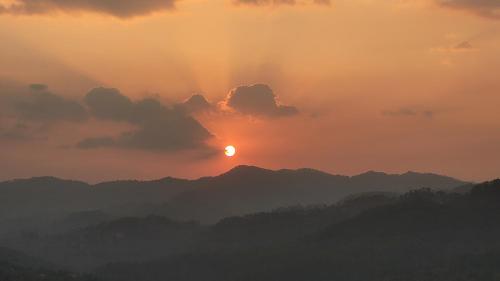 a sunset over a mountain range with the sun hiding behind clouds at Mahi Restaurant & Guest House in Almora