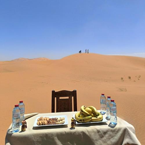 a table in the desert with a plate of food at Merzouga Horizon Luxury Camp in Merzouga