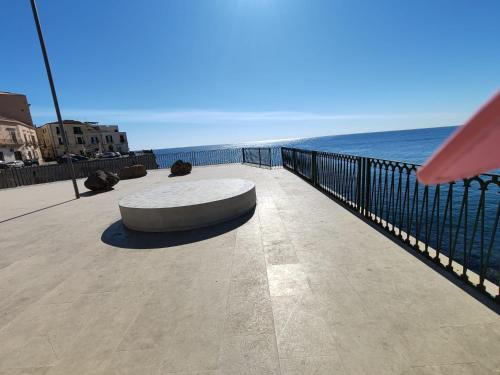 a bench on a sidewalk next to the ocean at Asturie Home in Siracusa