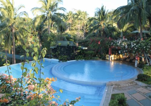 a large swimming pool with palm trees in the background at Magarra Hotel in Orani