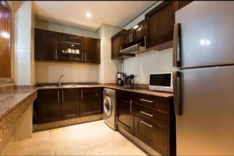 a kitchen with wooden cabinets and a stainless steel refrigerator at Élégant Appartement de Standing à la Marina in Agadir